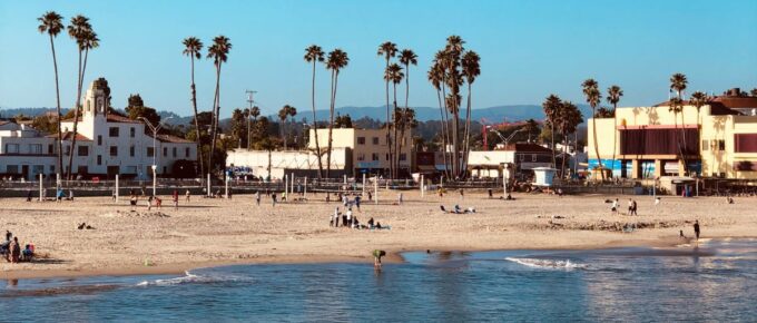Santa Cruz Beach in California with palm trees, people, and buildings around during the day.