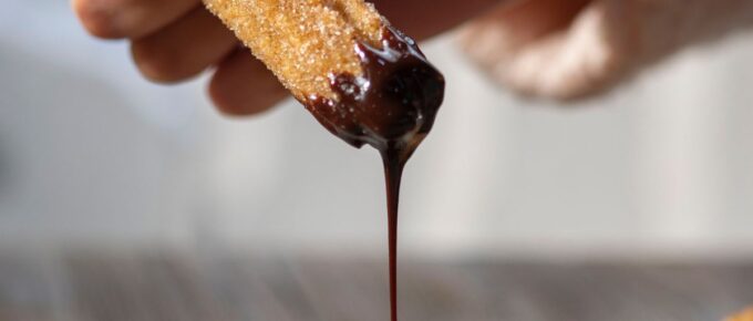 A woman holding churro while chocolate drips.