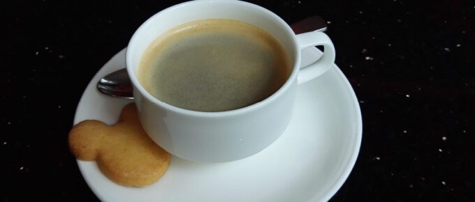 White cup with black coffee and Mickey Mouse shaped cookie.
