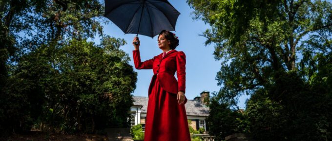 Marry Poppins, wearing a red dress and holding a black umbrella.