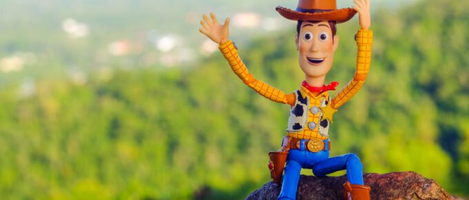 Woody of Toy Story movie sitting on the rock waving.