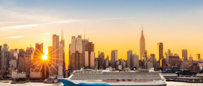 A large cruise ship sails Hudson river in New York while sun beams burst between the skyscrapers.
