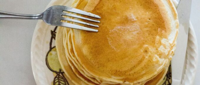 Pile of pancakes on a white plate with knife and fork.