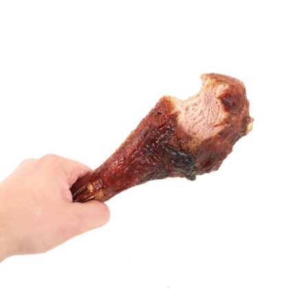 Hand holding roasted chicken leg with bite taken, isolated on white background.