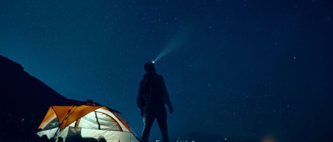 Man standing beside camping tent wearing headlamp while stargazing.