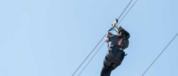 Back of one young American woman isolated against a blue sky on a zipline.
