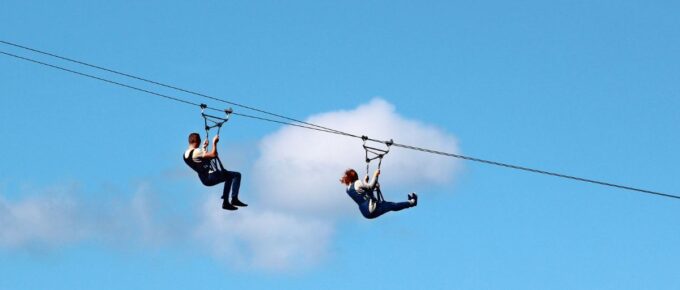 Man and woman descend on a zipline during day time.